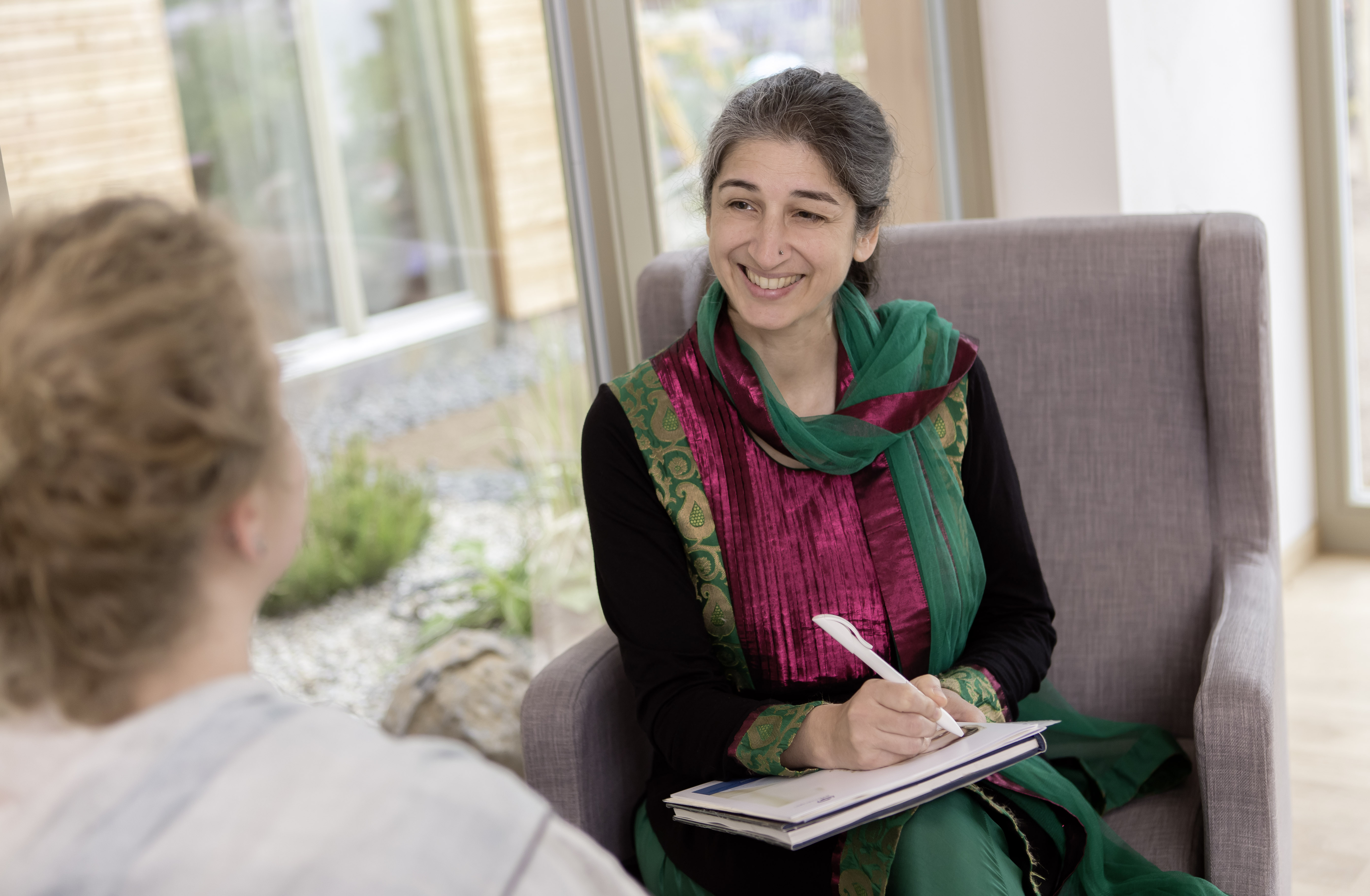 Ayurveda-Ärztin im Gespräch mit einer Patientin, Stethoskop und Fachbuch auf dem Tisch