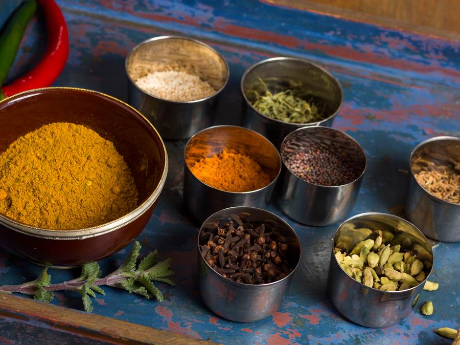 Ayurvedische Gewürze in Edelstahldosen: Kurkuma, Senfsaat, Kreuzkümmel, Nelken und Kardamom